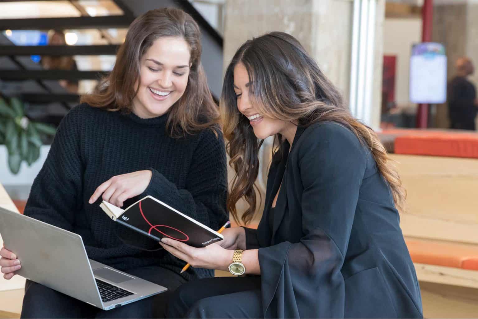 Two women working together with a laptop and tablet at a coffee shop.