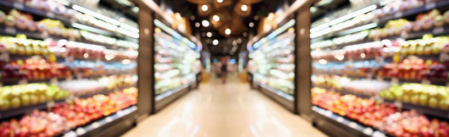 Empty grocery store aisle with well-stocked produce sections on both sides.